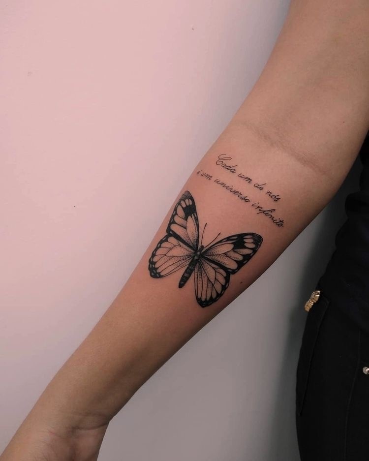 Tatuagem de borboleta e frase "cada um de nós é um universo infinito" no braço