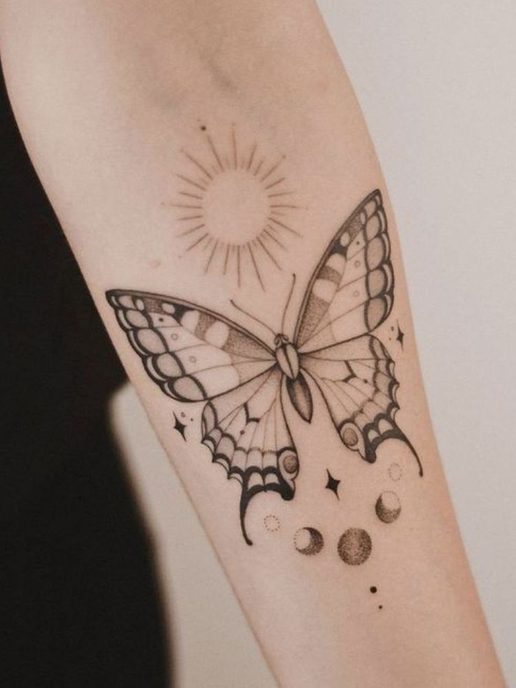 Foto de tatuagem de borboleta, com sol e fazes da lua no antebraço.