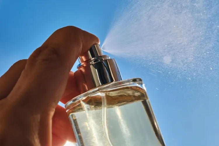 Mão de pessoa espirrando perfume para o verão em céu azul