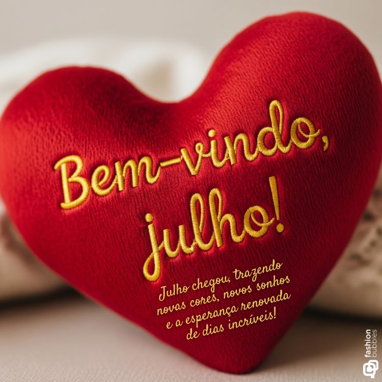 A imagem exibe um coração de pelúcia vermelho com a frase "Bem-vindo, Julho!" bordada em amarelo. Abaixo, há um texto menor que diz: "Julho chegou, trazendo novas cores, novos sonhos e a esperança renovada de dias incríveis!".

