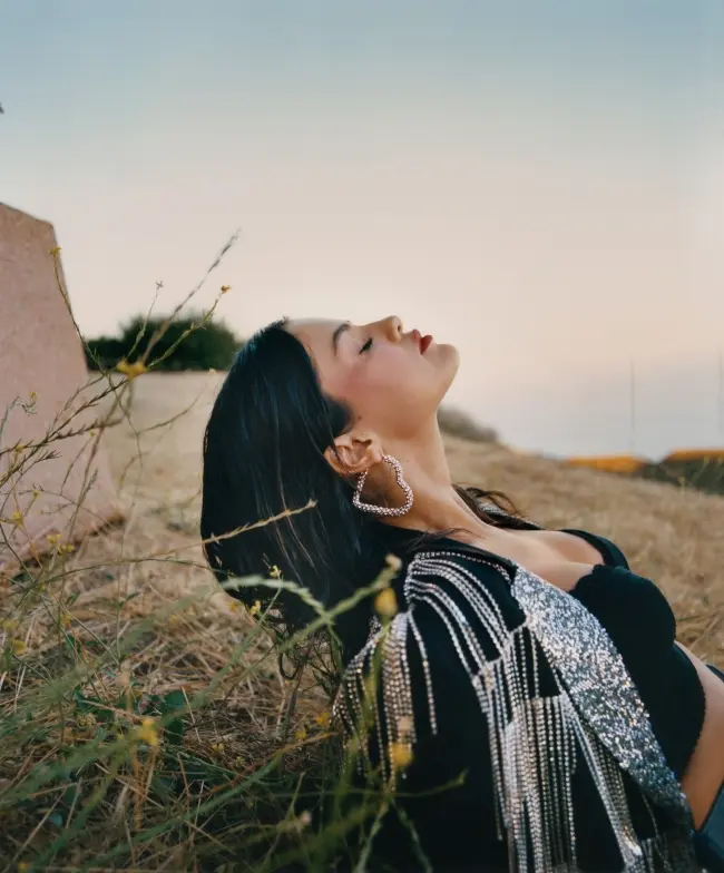 Frase para foto pensativa Selena Gomez deitada na grama usa top preto, blazer com brilho e strass e brinco de coração