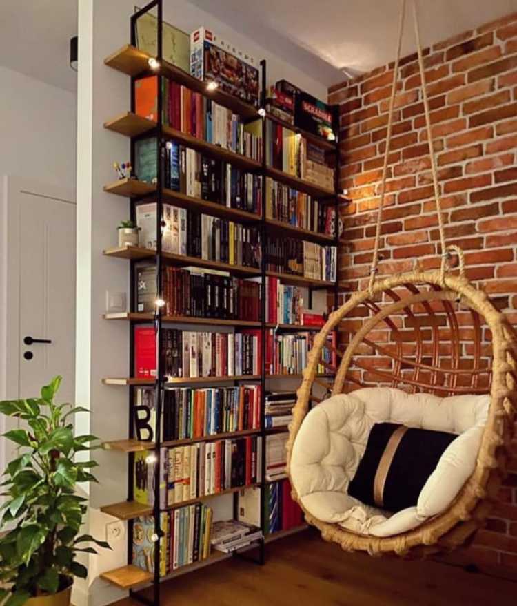 canto com parede de tijolos, balanço de madeira e estante preta com livros