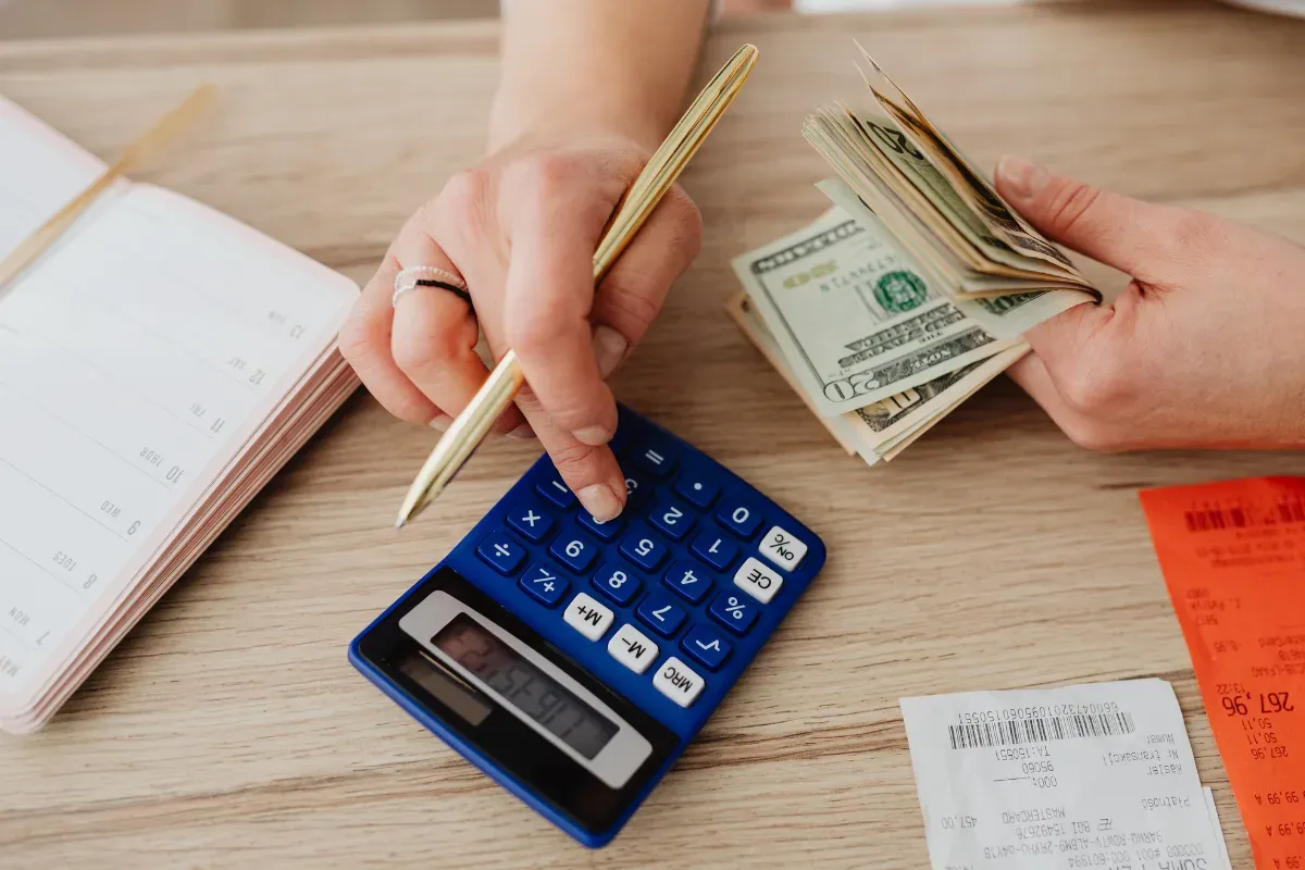Pessoa usando calculadora enquanto segura notas de dólar e organiza despesas