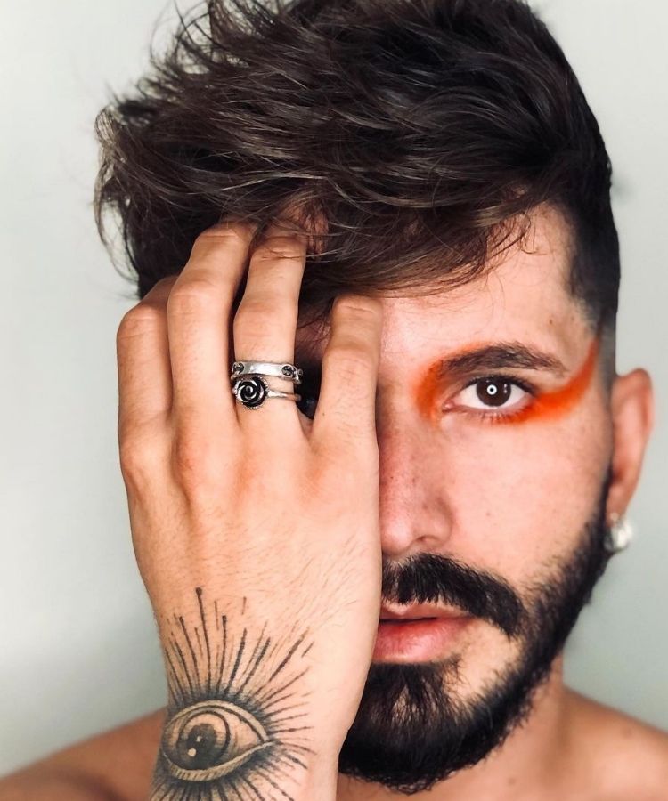 Homem de pele clara com mão no rosto e delineado laranja