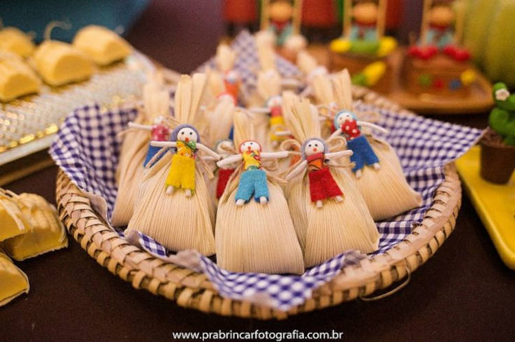 A imagem representa pamonhas decoradas com espantalhos em peneira de palha com tecido xadrez