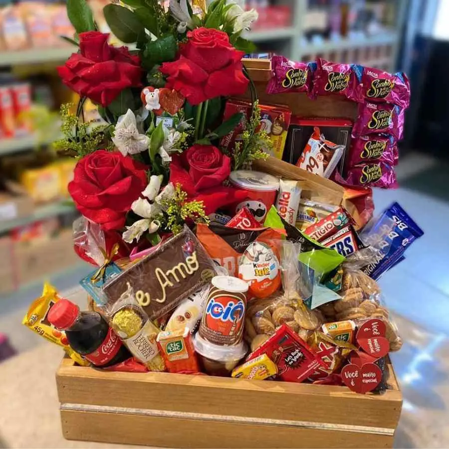 Foto de caixote com rosas recheado de doces, balas e bebidas.