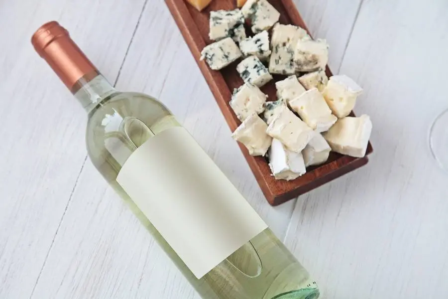 garrafa de vinho branco ao lado de tábua de queijos
