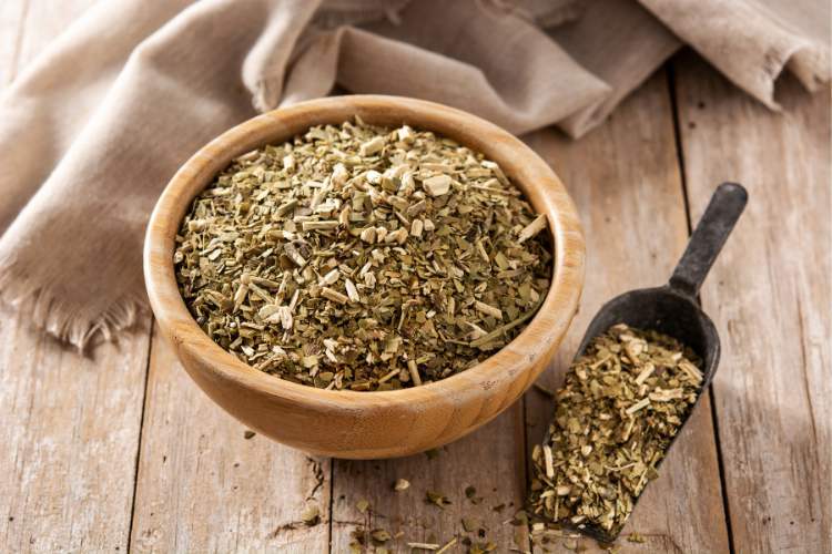 Tigela de madeira com erva-mate em mesa de madeira com tecido e colher de ferro com a erva também