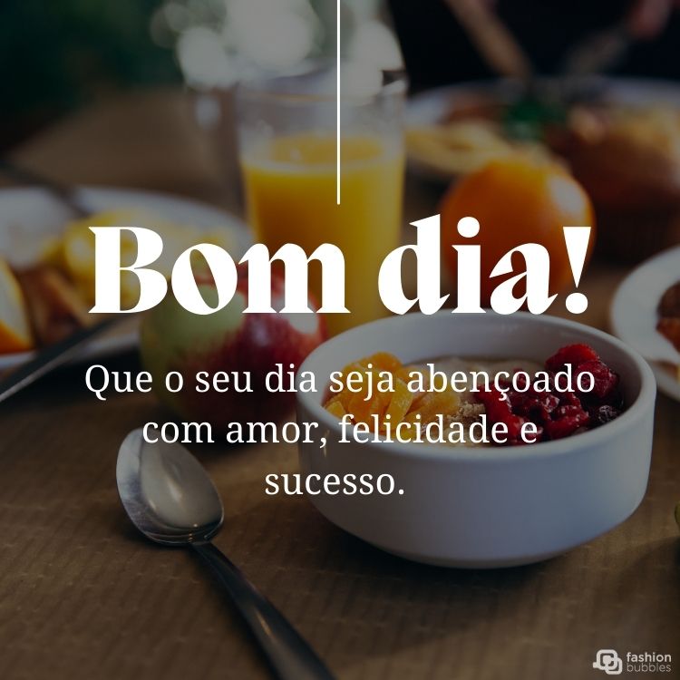 Foto de café da manhã com tigela de frutas, suco, colher e frase: Que o seu dia seja abençoado com amor, felicidade e sucesso. Bom dia!