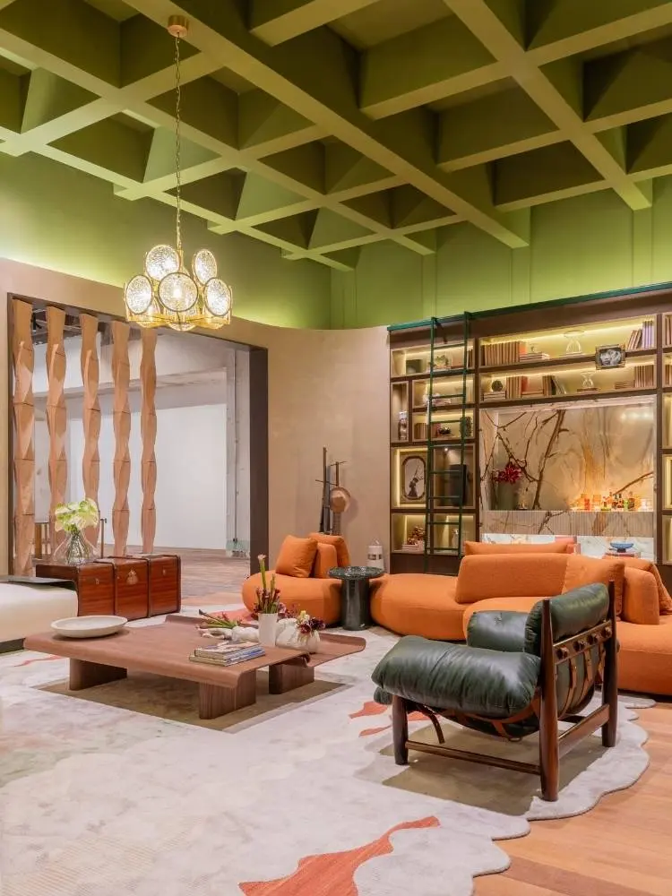 Sala de estar com teto envelopado em gesso em verde, lustre, tapete claro, sofá laranja, estante ao fundo, poltronas escuras