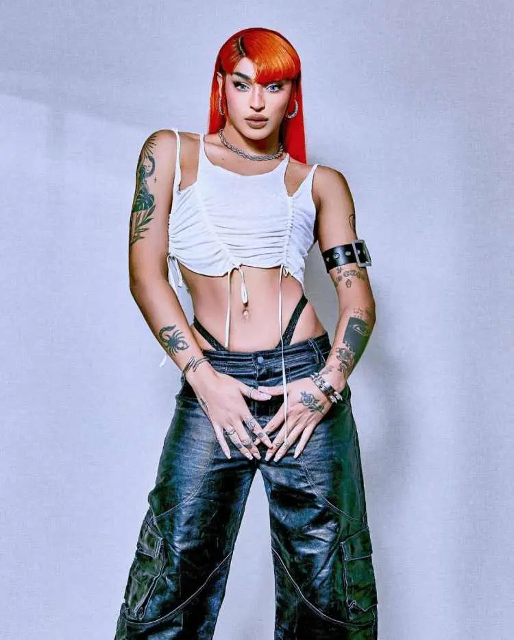 Pabllo Vittar com top branco e calça couro em fundo branco exibindo tatuagens nos braços, pulsos e mão 