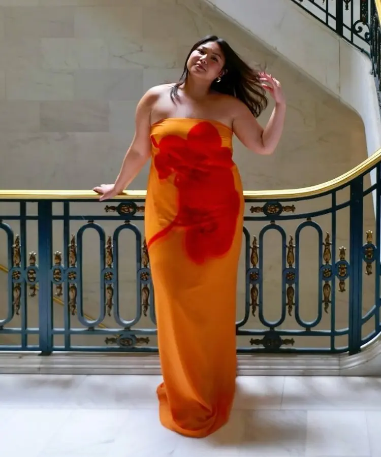 Mulher usando vestido longo sem alças laranja com estampa de flor vermelha
