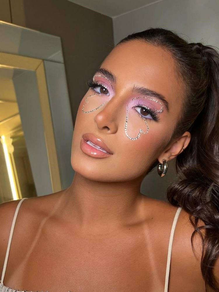 Mulher de pele clara com maquiagem rosa e borboleta feita de strass 