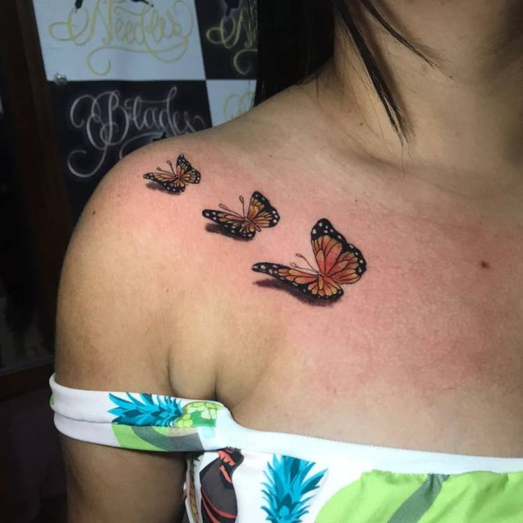 Mulher de pele clara e blusa verde com tatuagem de três borboletas laranjas de tamanho crescente no ombro