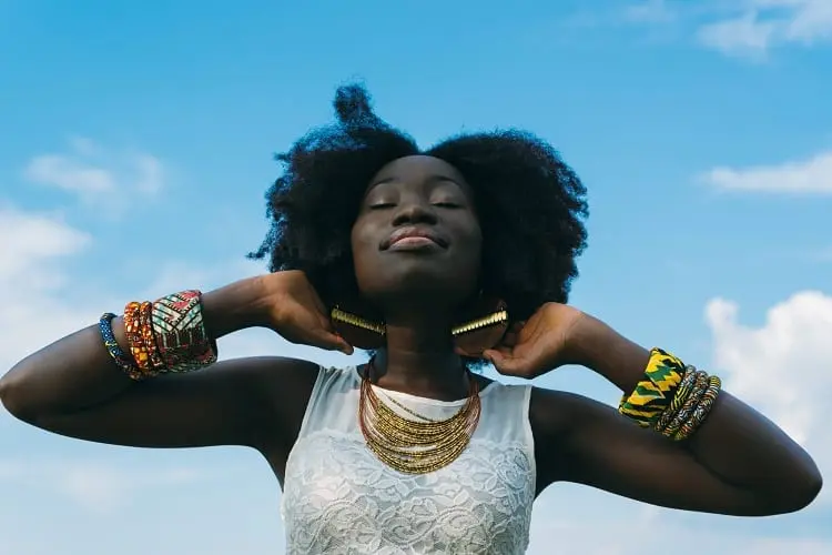 moça de pele negra e olhos fechados sorrindo com um céu azul ao fundo
