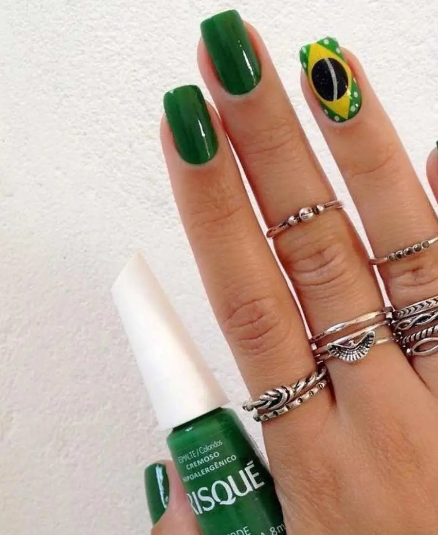Imagem de mão decoradas com esmalte.  Cores usadas, verde, amarelo, azul e branco. Polegar: verde. Indicador: verde. Dedo Médio, verde. Anelar: verde com bandeira e bolinhas brancas. Mínimo: verde.