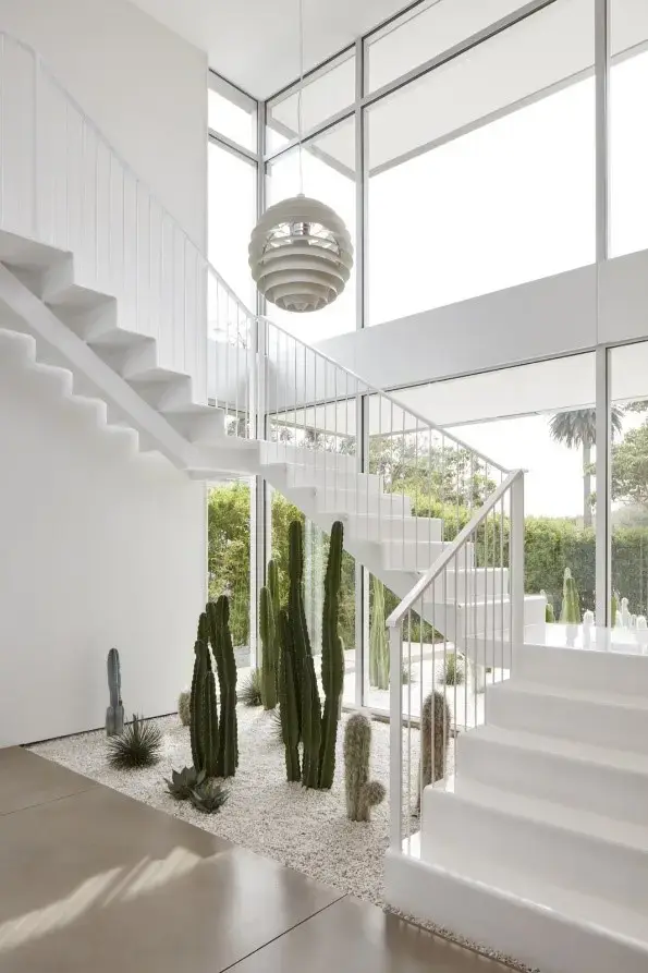 Jardim de inverno com cactos e outras suculentas embaixo da escada branca.