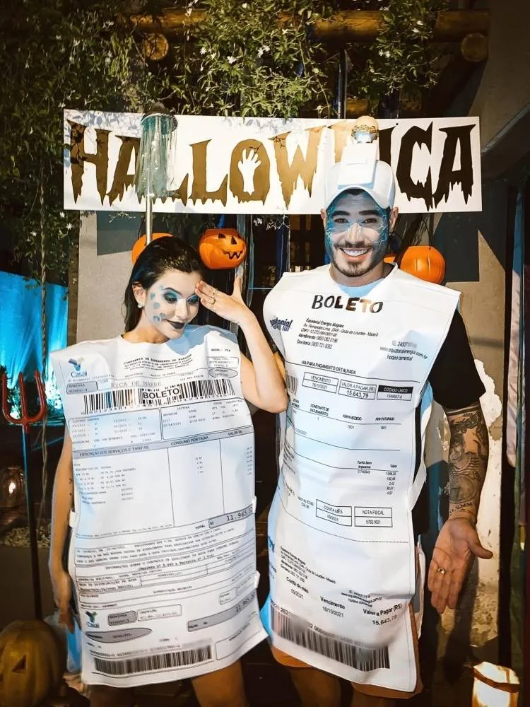 Casal de influenciadores Rica de Marré e Adrão Meron fantasiados de boleto para o Halloween: ela usa maquiagem pálida com detalhes em azul, imitando água. Já ele usa maquiagem pálida com raios, boné branco com espelho de tomada e boleto 