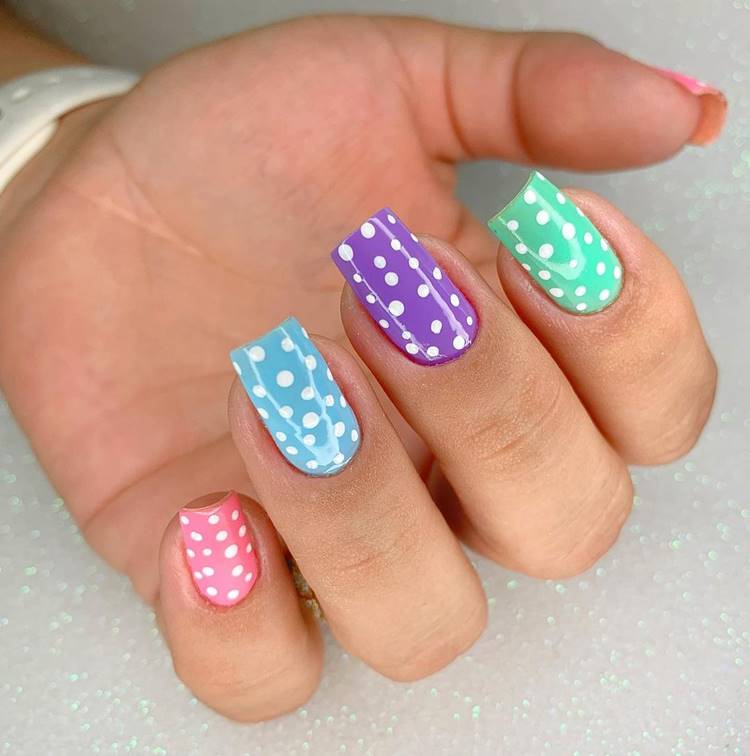 Mão com unhas arco-íris LGBTQIA+: Polegar: rosa com bolinhas brancas Indicador: verde com bolinhas brancas Médio: roxo com bolinhas brancas Anelar: azul com bolinhas brancas Mínimo rosa com bolinhas brancas