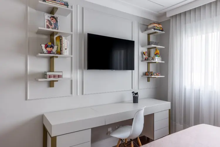 Foto de parte do quarto com mesa, cadeira, estante com decorações, televisão e parede clara com boiserie 