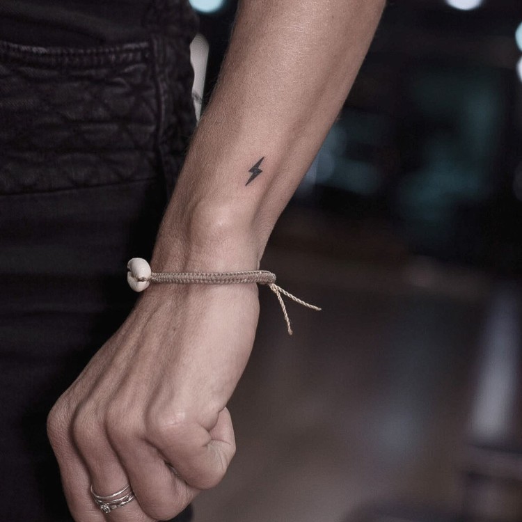Tatuagem pequena e preenchida de raio no pulso 