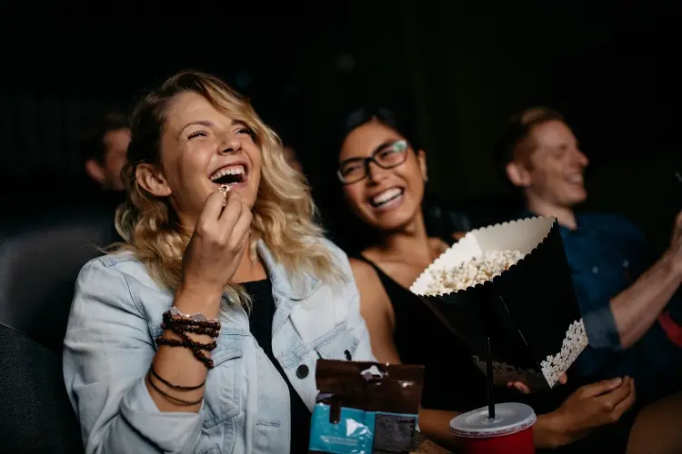 Foto de duas mulheres rindo e comendo pipoca, vendo filme no cinema 