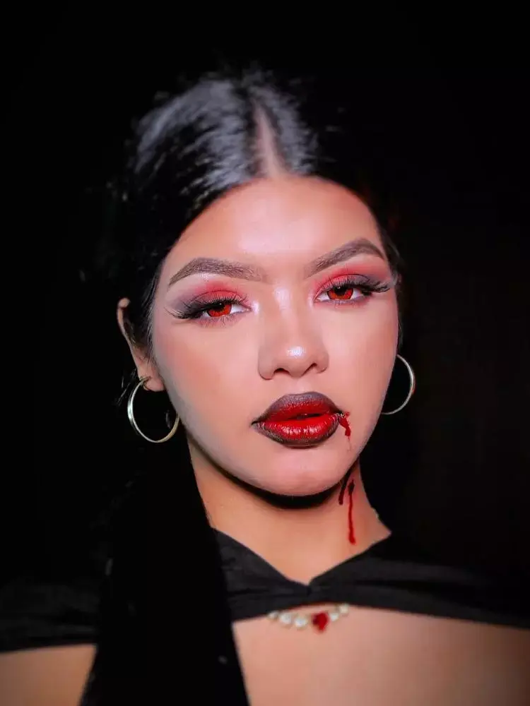 Mulher de pele morena com sombra vermelha, batom vermelho e sangue escorrendo da boca