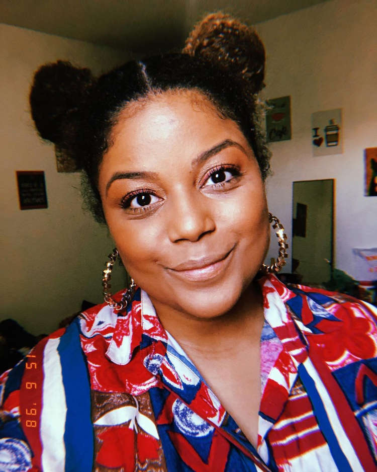 Mulher de pele negra com cabelo cacheado castanho escuro preso em dois coques