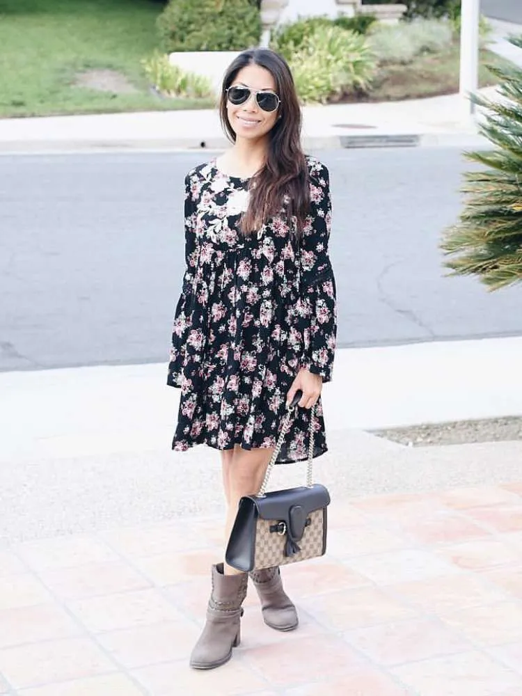 Mulher de pele clara com vestido curto de manga longa preto com flores 
