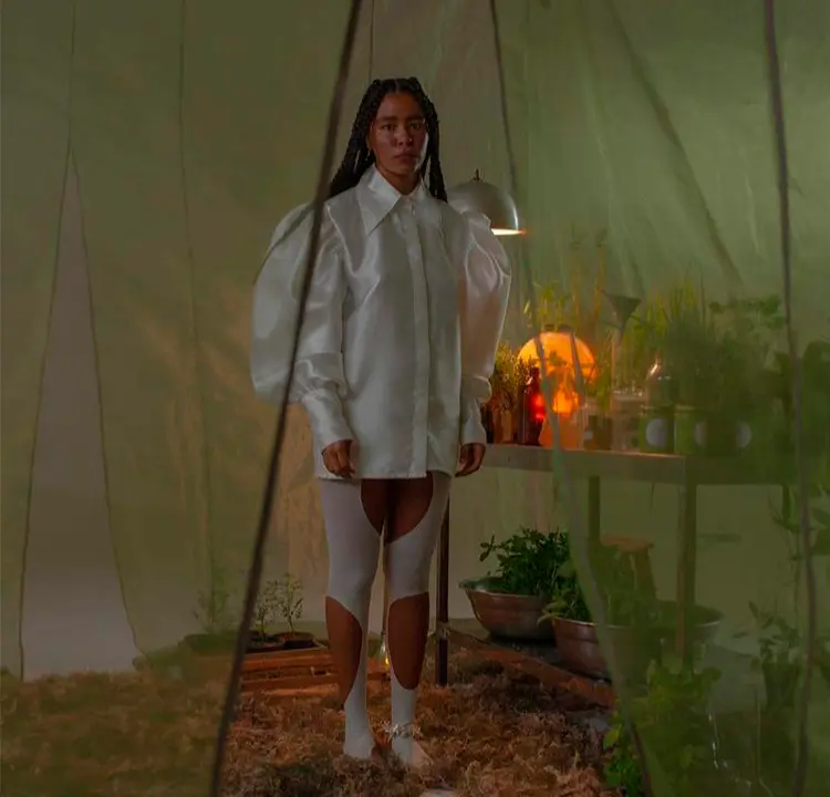 Modelo com blusa de mangas bufantes branca em ambiente verde cheio de plantas.
