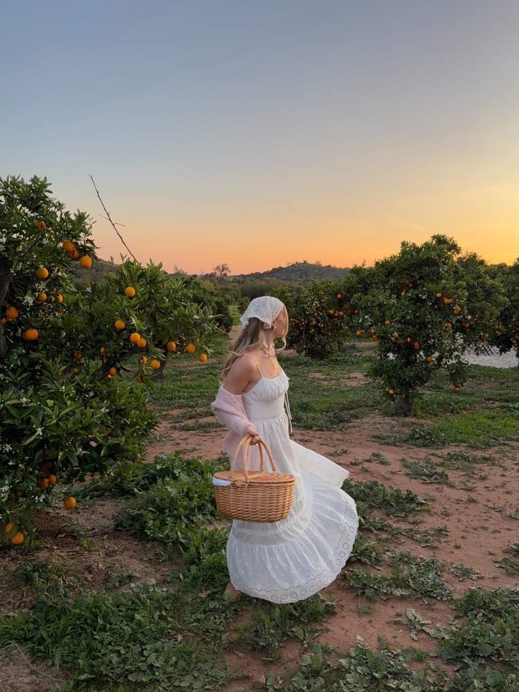 Mulher de pele clara no campo usando vestido fluido, cardigan rosa claro 