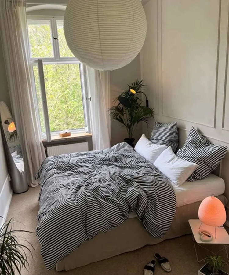 Quarto de casal com espelho oval no canto de parede. Cores predominantes: preto, branco, off-white