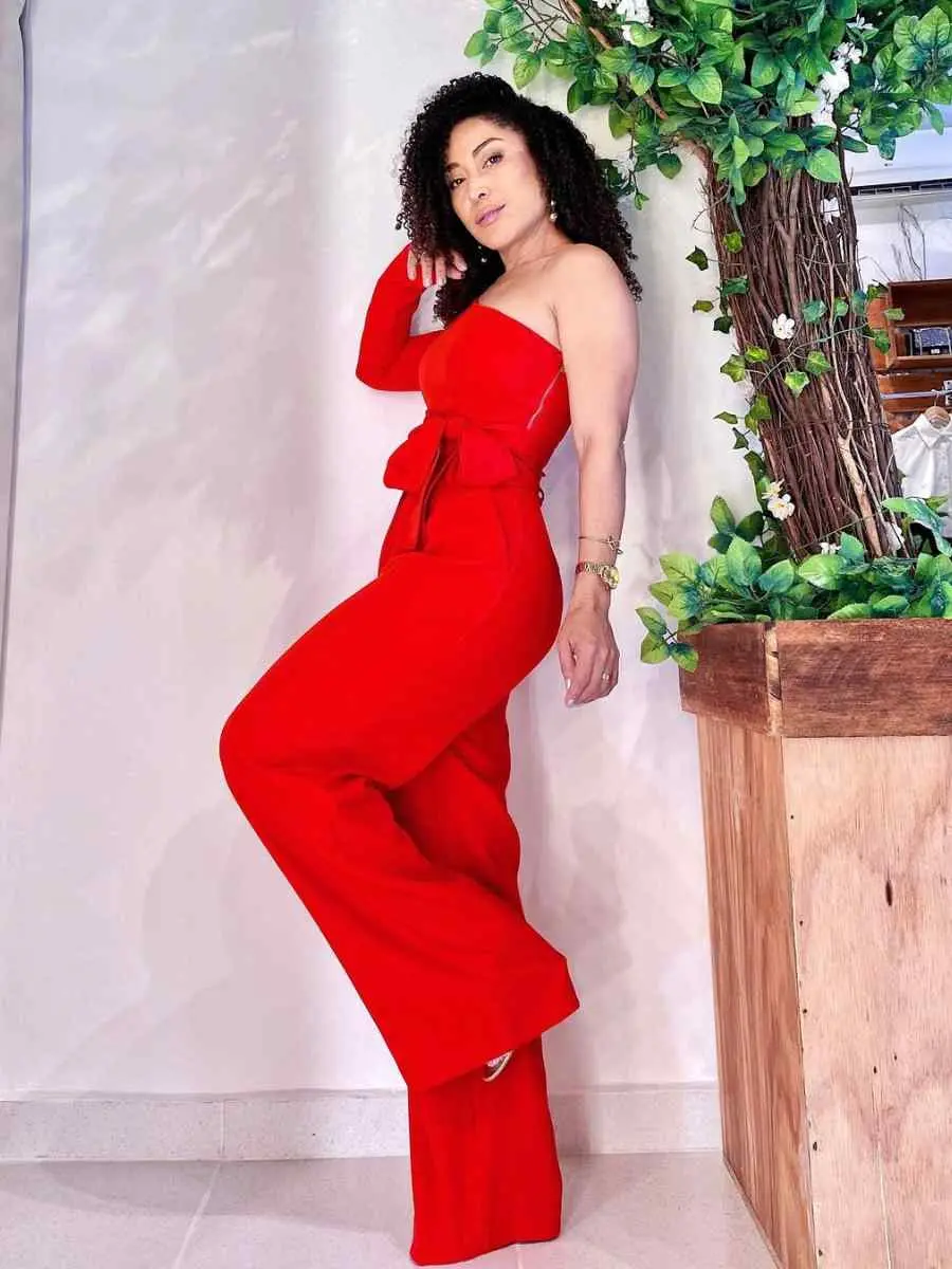 Mulher usando look all red composto por macacão de uma manga só, laço e barra larga.