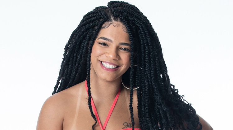 Foto de Maria em fundo claro usando blusa coral de amarração no pescoço