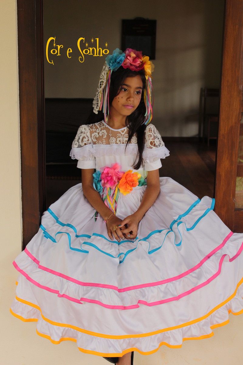 Menina de pele morena com vestido rodado de noivinha de festa junina e adereços coloridos no cabelo 