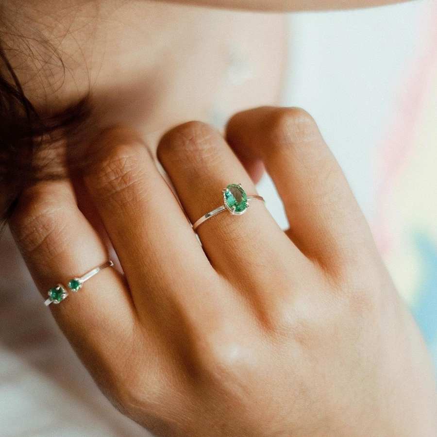 Mulher de pele clara usando dois anéis delicados com pedra verde