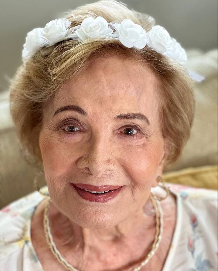 Glória Menezes hoje em dia, maquiada, usando coroa de flores na cabeça