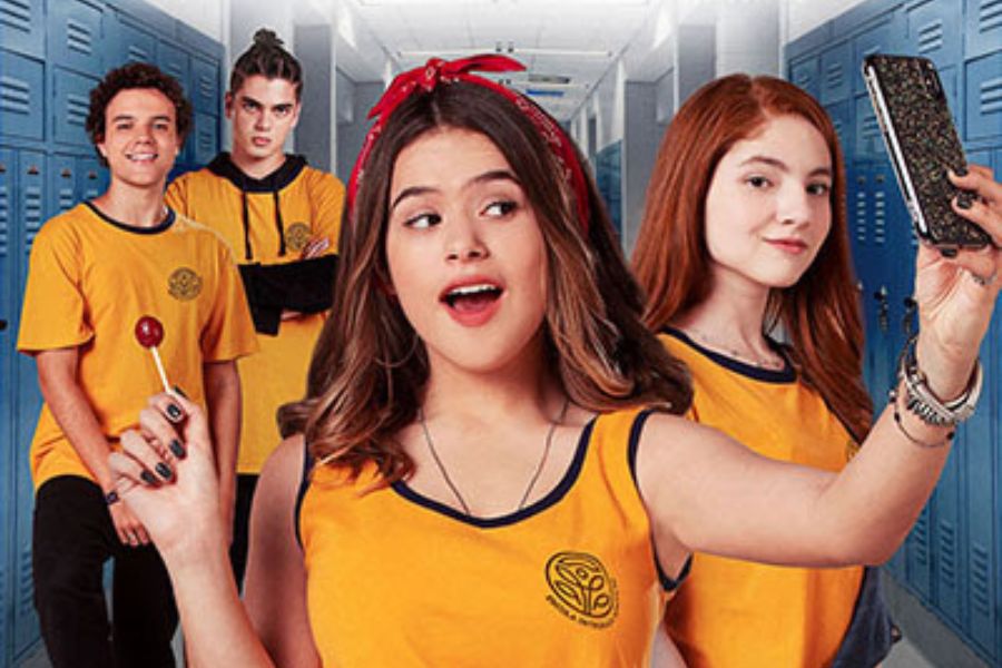 Foto de Maísa (Julia), Giulia Ayumi (Carol), Marcus Bessa (Léo) e Matheus Lustosa (Rafa) de "Ela Disse, Ele DIsse". Todos estão em corredor de uma escola com armários. Maísa está na frente, segurando pirulito e tirando selfie com os demais.