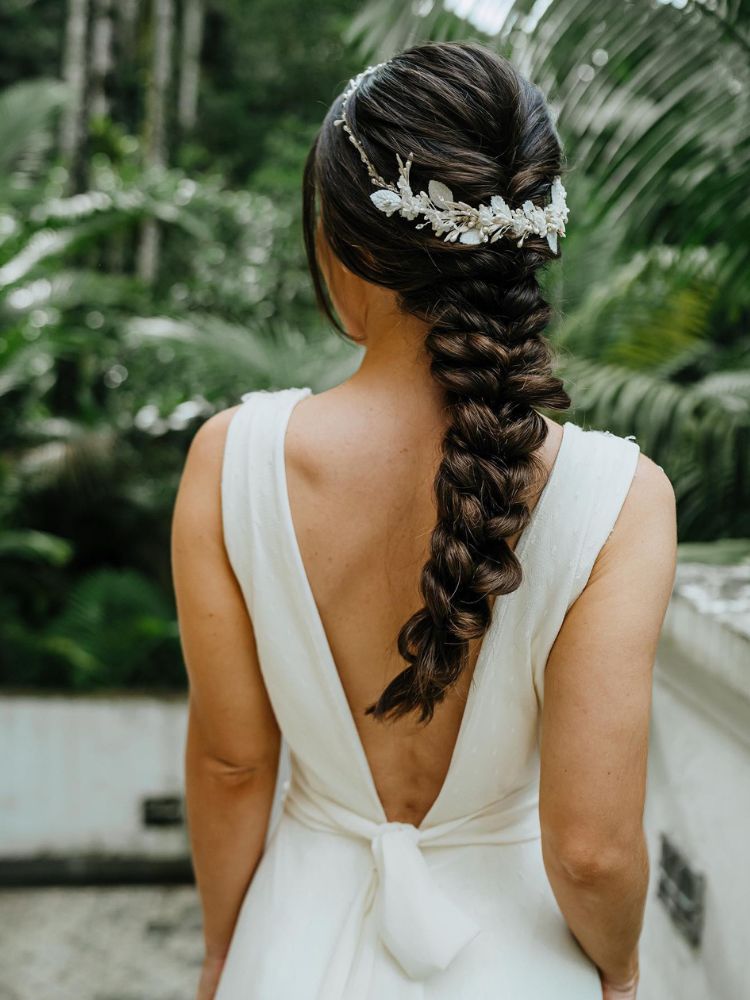 Mulher de pele clara de costas usando vestido de noiva e cabelo inteiro trançado e com acessório