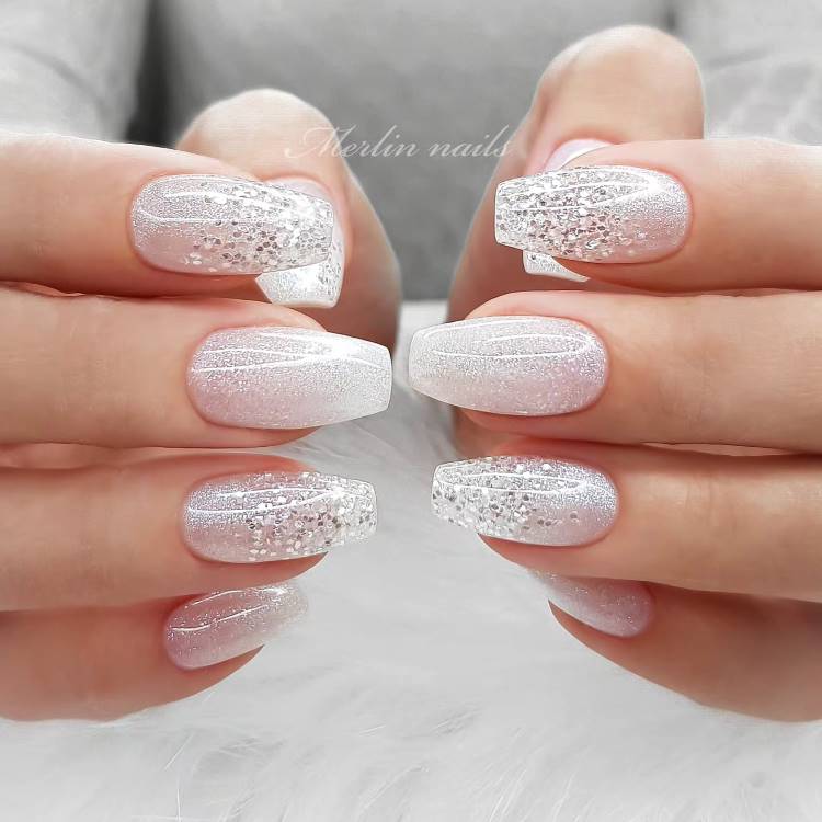 Mãos femininas com unhas em formato oval, decoradas com esmalte perolado e detalhes dourados minimalistas. Anéis delicados, incluindo um com pedra central, complementam o visual elegante. O fundo neutro realça a sofisticação e o brilho das unhas.





