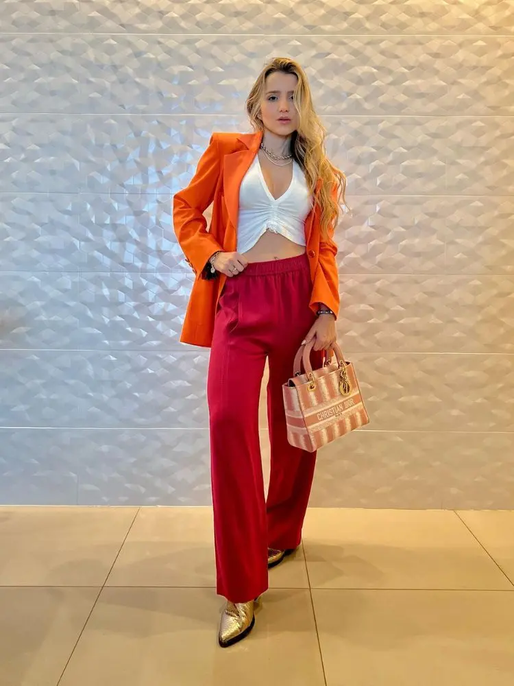 Mulher de pele clara usando cropped branco, blazer laranja e calça vermelha