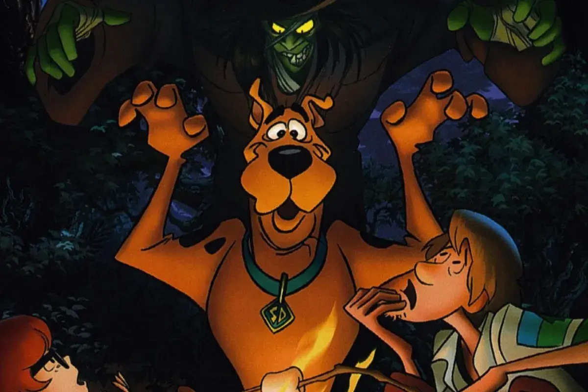 Scooby-Doo e Salsicha assustados durante acampamento noturno cercado por criatura misteriosa na floresta.