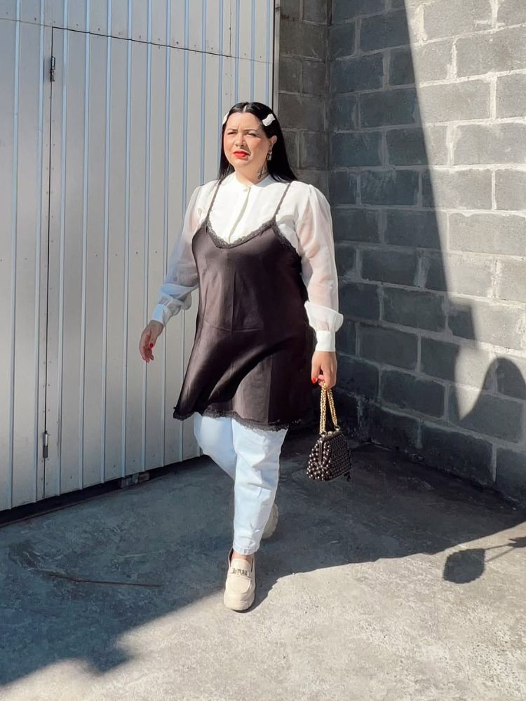 Mulher de pele clara usando camisa branca, slipdress preto, calça azul clara 