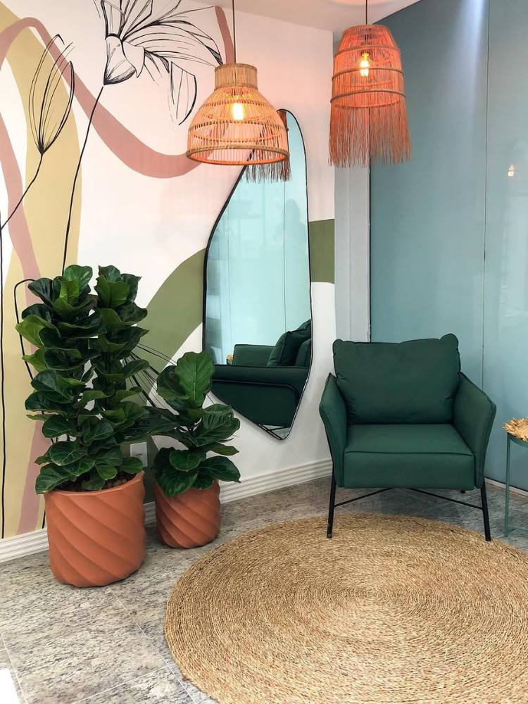 Hall com parede colorida, poltrona verde, dois vasos beges de Ficus Lyrata e tapete redondo 