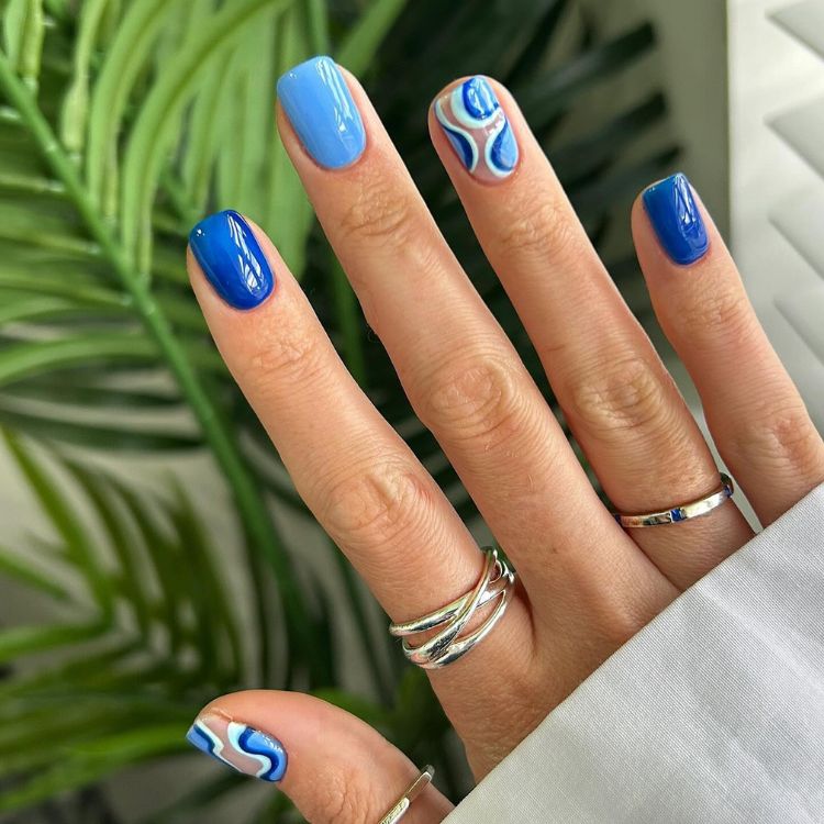 Unhas em mix de azul com dedão e anelar em nude com branco e azul abstrato