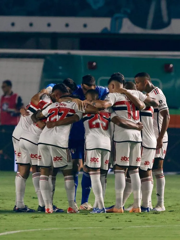 Elenco do São Paulo com primeiro uniforme (branco) se abraçando no gramado. 
