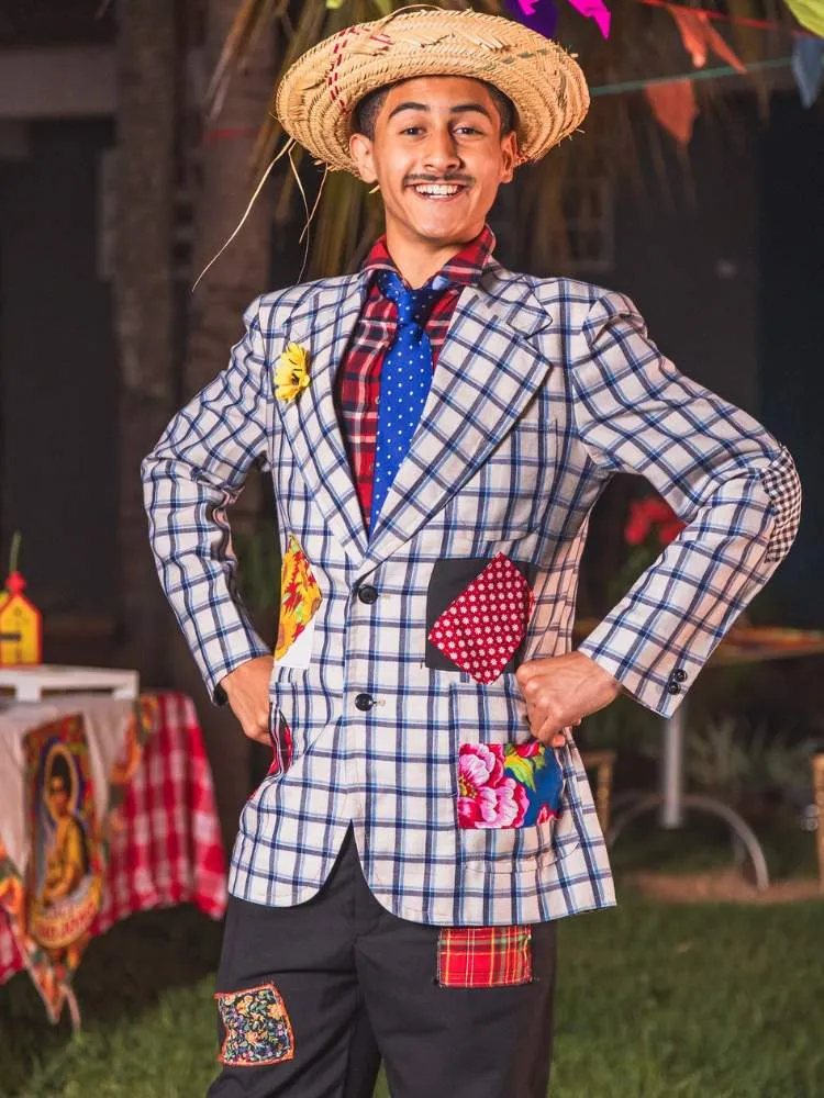 Homem de pele clara com chapéu de palha, camisa xadrez com retalhos e calça também com retalhos 