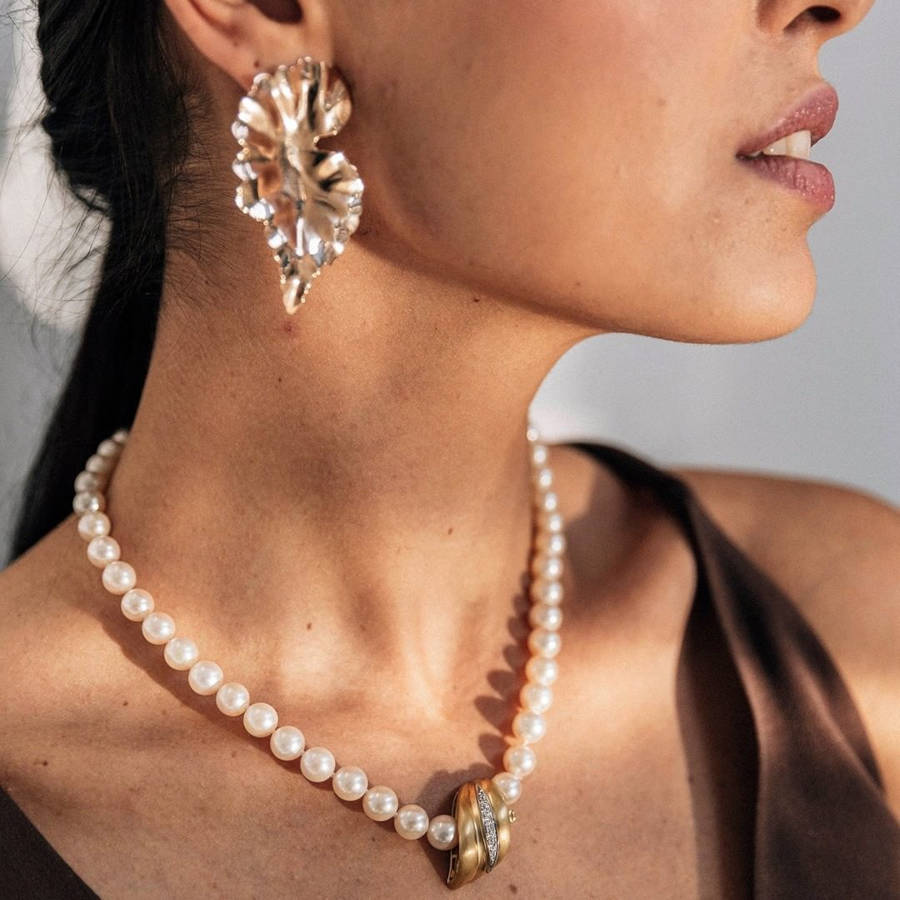 Modelo posa para a marca de joias secondhand Orit com cordão de pérolas e pingente de ouro e brilhante e brinco de ouro em formato de folha