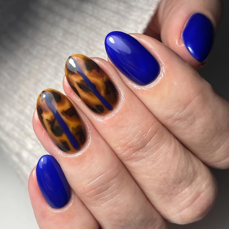 Unhas redondas em azul escuro com anelar e médio em onça com faixa azul