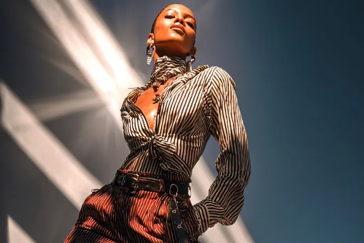 Foto de modelo negra careca usando brincos grandes e camisa listrada